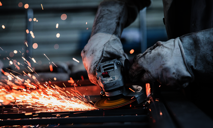 Nahaufnahme eines Handwerkers mit Schutzhandschuhen beim Bearbeiten von Metall mit einem Winkelschleifer und Funkenflug